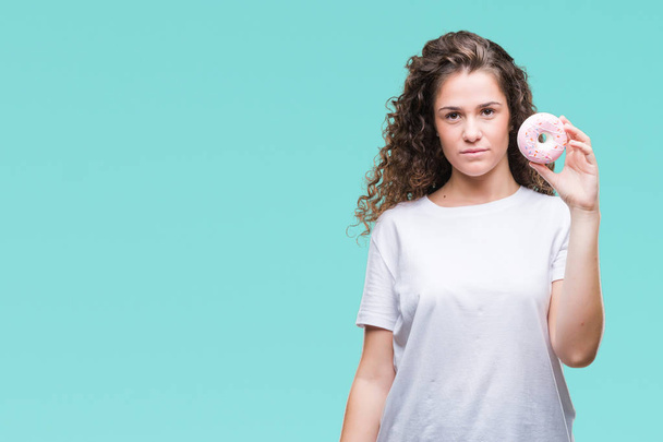 Young brunette girl eating donut over isolated background with a confident expression on smart face thinking serious - Fotó, kép