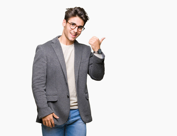 Young business man wearing glasses over isolated background smiling with happy face looking and pointing to the side with thumb up. - Foto, Imagen