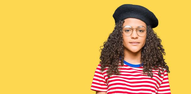 Young beautiful woman with curly hair wearing glasses and fashion beret Relaxed with serious expression on face. Simple and natural looking at the camera. - Photo, Image