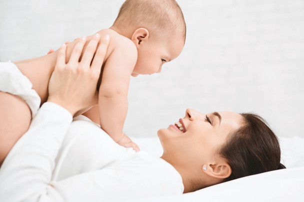 Fiatal anyuka tartja a boldog baba, levegőben - Fotó, kép