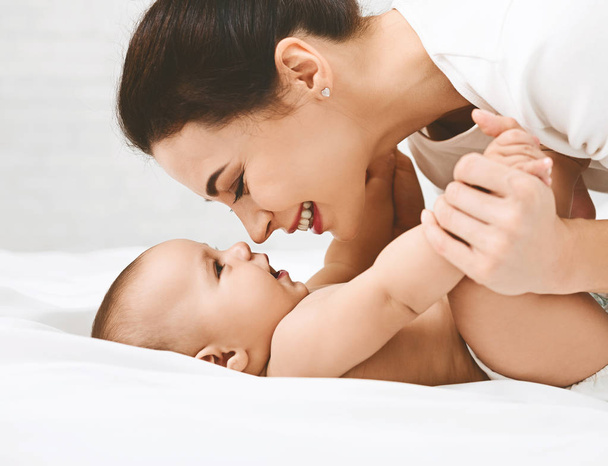 Jeune femme jouant avec son petit bébé au lit
 - Photo, image