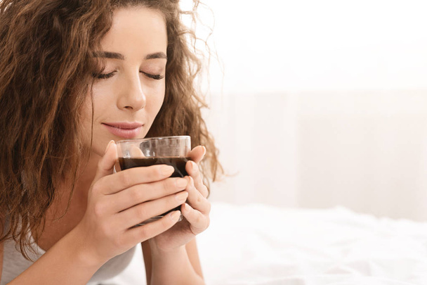 Jonge vrouw ontspannen op bed met koffie - Foto, afbeelding