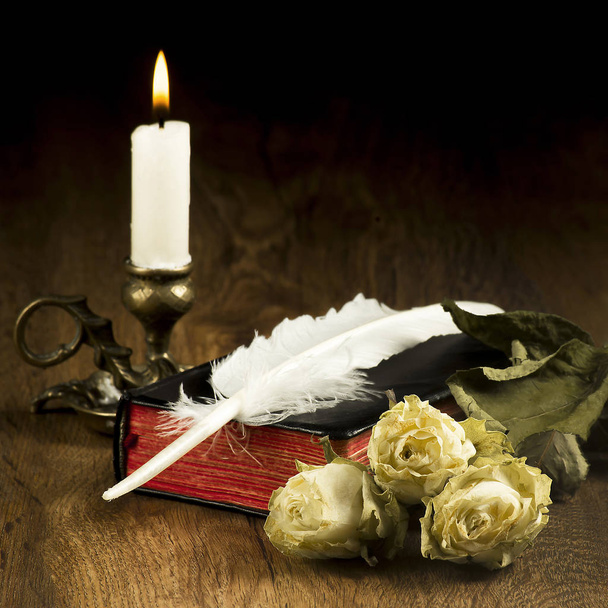 old books, dead roses, a burning candle and a feather on the boards - Foto, Imagen