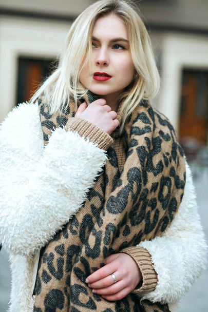 Closeup portrait of blonde woman with red lips wearing coat and scarf walking at the city - Photo, Image