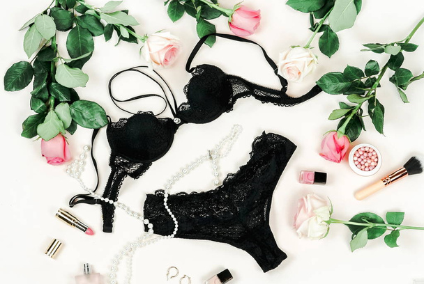 top view of black lingerie, pink roses and makeup equipment on white backdrop - Фото, изображение