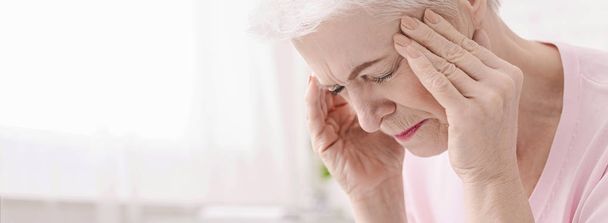 Mujer mayor con dolor de cabeza y tocando sus sienes
 - Foto, imagen