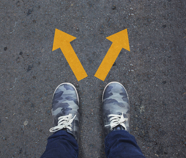 Pair of shoes standing on a tarmac road with two arrows directions, concept - Photo, Image