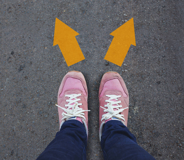 Par de zapatos de pie en una carretera asfaltada con dos flechas direcciones, concepto
 - Foto, imagen