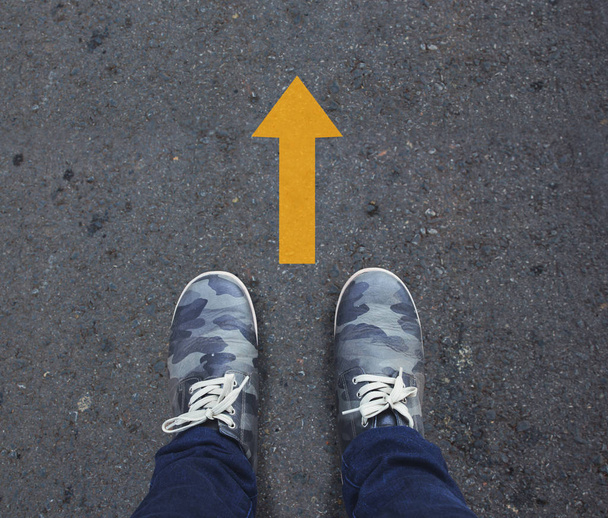Paar Schuhe stehen auf einer asphaltierten Straße mit gelbem Pfeil. - Foto, Bild