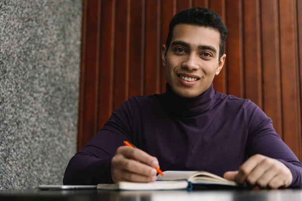 Mosolygó afro-amerikai egyetemista tanul, angol nyelvet tanul, jegyzetel a jegyzetfüzetben, dolgozik. Vegyes fajú férfi olvasókönyv, vizsgakészítés a könyvtárban. Oktatási koncepció - Fotó, kép