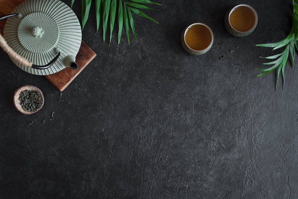 Teapot and Teacups on black background, copy space. Traditional Asian arrangement  for Tea ceremony -  iron teapot and ceramic teacups with tea, top view. - Fotó, kép