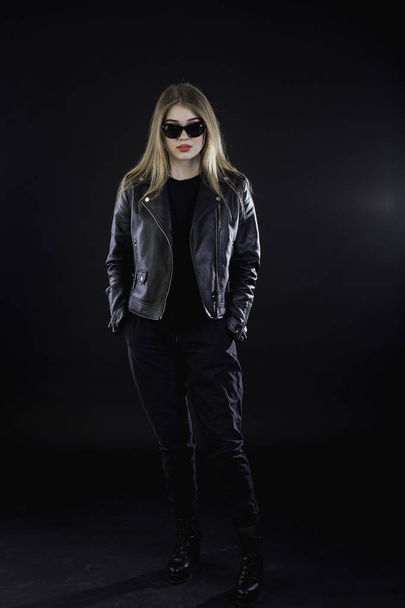 young girl in a black leather jacket and sunglasses on a dark ba - Foto, Imagen
