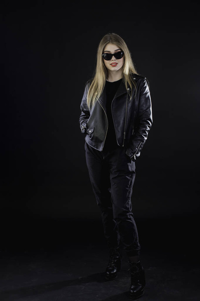 young girl in a black leather jacket and sunglasses on a dark ba - Фото, зображення