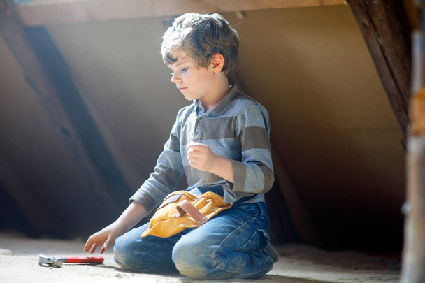 Kleiner Junge hilft mit Spielzeug auf Baustelle. Lustiges Kind von 6 Jahren, das Spaß am Bau eines neuen Familienhauses hat. Kind mit Nägeln und Hammer hilft Vater bei Renovierung von altem Haus. - Foto, Bild