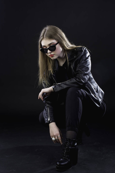 young girl in a black leather jacket and sunglasses against a da - Foto, imagen