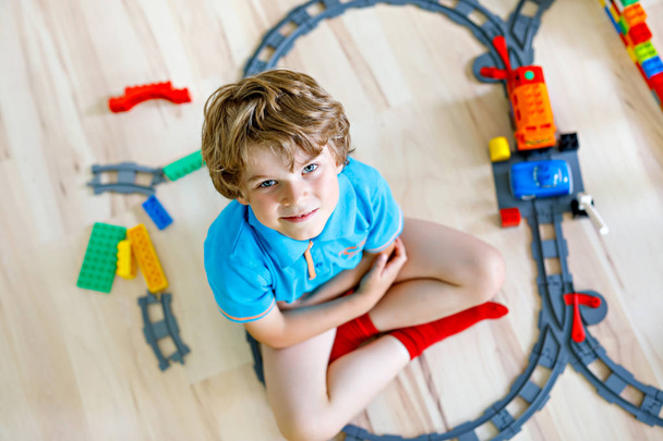 愛らしい小さな金髪の子供男の子カラフルなプラスチック製のブロックで遊んでいると駅を作成します。鉄道おもちゃ自宅の建物との楽しみを持っている子供 - 写真・画像