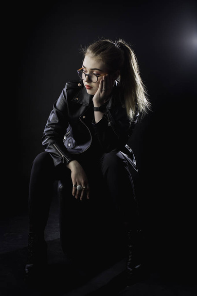 young girl in a black leather jacket and glasses on a dark backg - Foto, Imagen