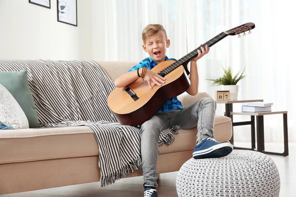 Cute little boy playing guitar on sofa in room - Zdjęcie, obraz