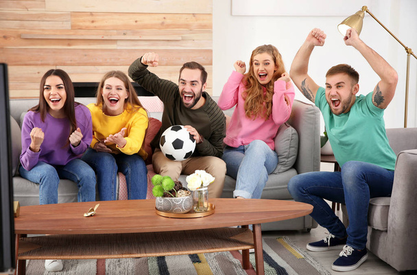 Group of friends celebrating victory of favorite soccer team in living room - Фото, изображение