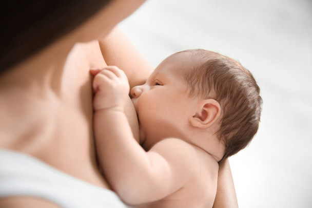 Young woman breastfeeding her baby on light background, closeup - Fotó, kép