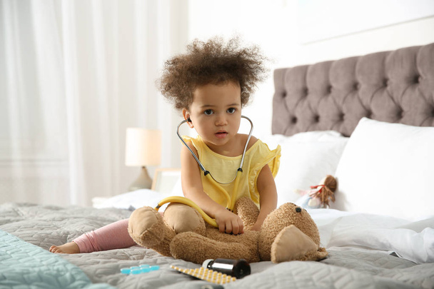 Słodkie dziecko African American, wyobrażając sobie siebie jako lekarz podczas gry z stetoskop i zabawka królik w domu - Zdjęcie, obraz