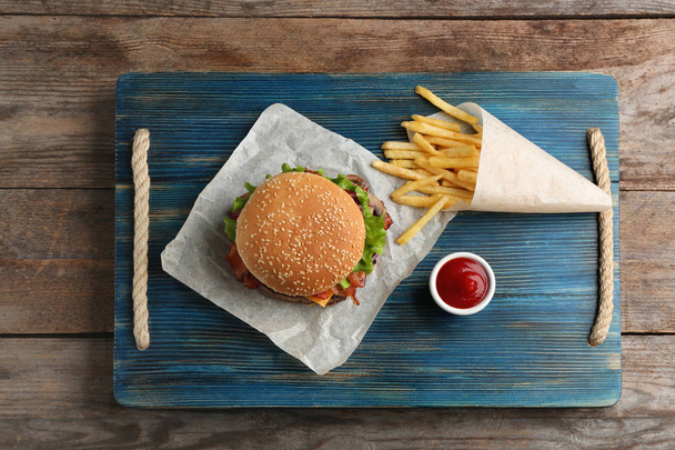 Tasty burger, french fries and sauce on wooden board, top view - 写真・画像