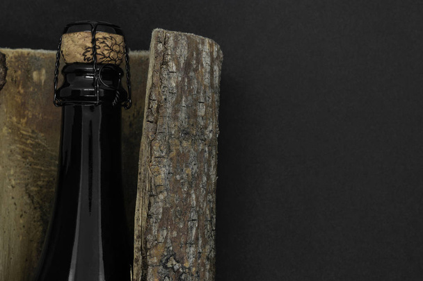 Ağaç kabuğu siyah arka plan üzerine yerleştirilen bej cork şampanya siyah cam şişe ile kapalı soyut kompozisyon - Fotoğraf, Görsel