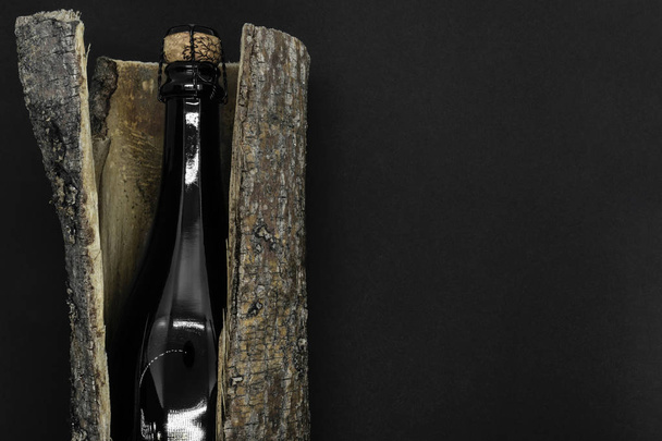 Composition abstraite de fermé avec du champagne en liège beige bouteille en verre noir placée dans l'écorce d'arbre sur fond noir avec espace de copie
 - Photo, image