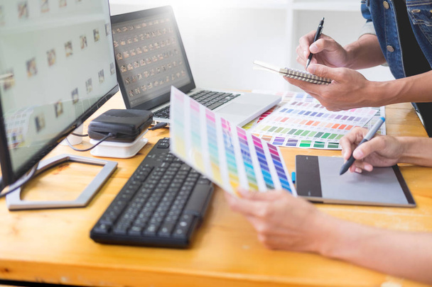γραφικός σχεδιαστής ομάδα εργασίας για web design με χρήση swatches χρώματος επεξεργασίας έργα τέχνης χρησιμοποιώντας tablet και μια γραφίδα στο γκισέ σε απασχολημένος δημιουργικό γραφείο - Φωτογραφία, εικόνα