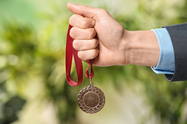 Man holding gold medal on blurred background, closeup - Foto, afbeelding