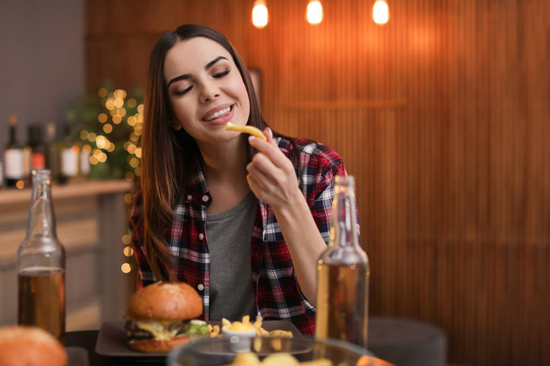 Young woman eating french fries and tasty burger in cafe. Space for text - Foto, imagen
