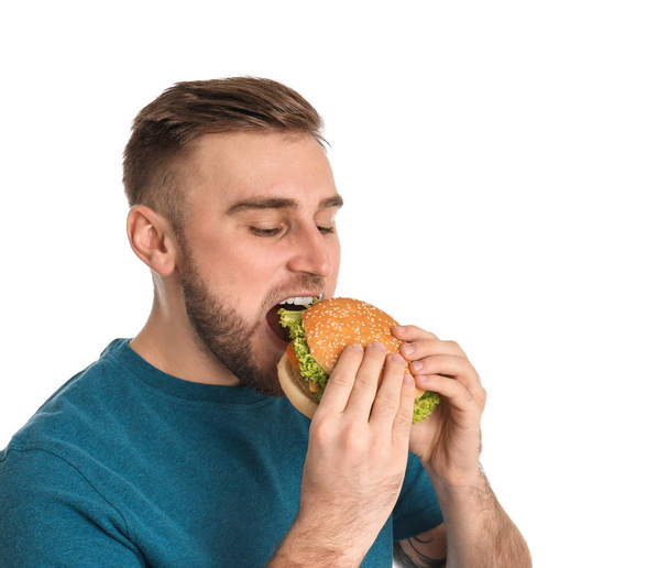 Jonge man eten smakelijke Hamburger op witte achtergrond - Foto, afbeelding