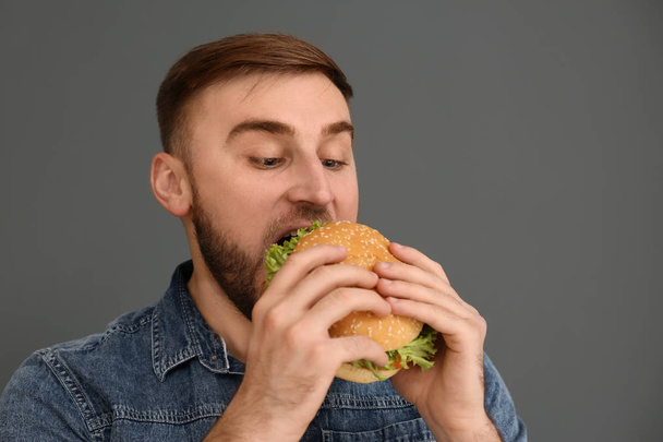 Young man eating tasty burger on grey background. Space for text - Fotoğraf, Görsel