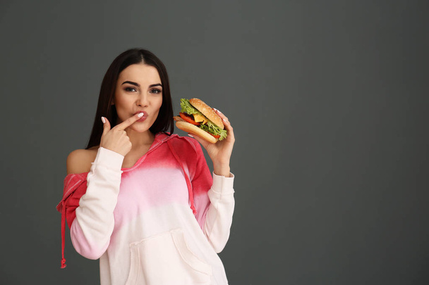 Young woman eating tasty burger on grey background. Space for text - Valokuva, kuva