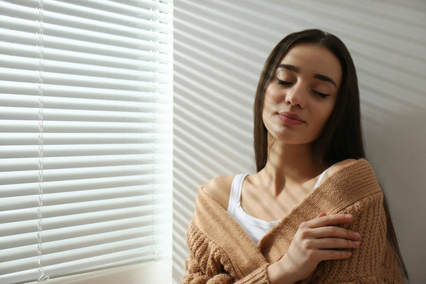 Young woman near window with Venetian blinds. Space for text - Foto, afbeelding