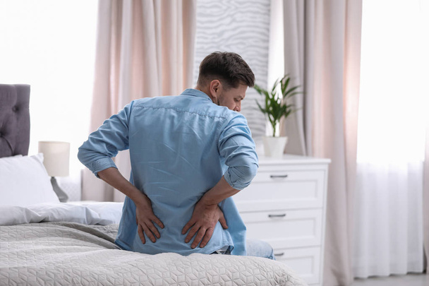Young man suffering from back pain at home - Fotó, kép