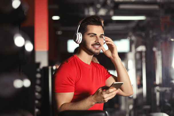 Young man with headphones listening to music on mobile device at gym - Foto, immagini
