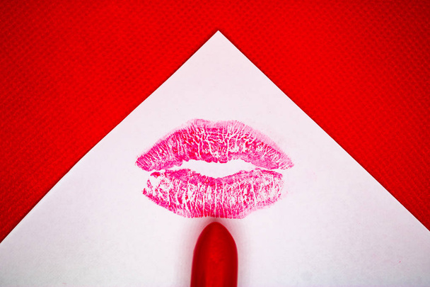Kussmarke und roter Lippenstift auf weißem Papier mit rotem Hintergrund - Bild - Foto, Bild