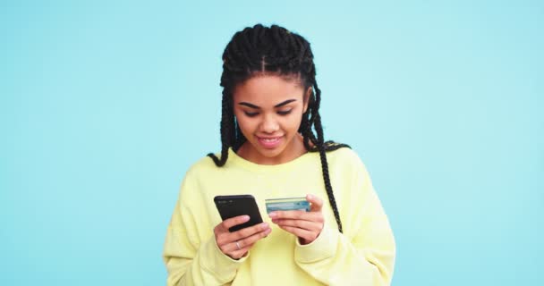 Good looking african woman make a online transaction with her smartphone , using the credit card , in a studio with a blue background wall - Imágenes, Vídeo