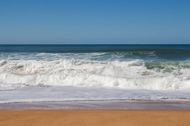 Limpiar la arena amarilla oscura de la playa de otoño. Color azul profundo del agua del océano Atlántico con olas espumosas. Horizonte en el fondo. Cielo azul claro. Playa de Lalla Fatna (Safi). Marruecos
. - Foto, Imagen