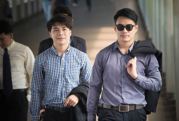Młody azjatycki biznesmen włożył kurtkę na ramię podczas spaceru z kolegą przed biurem - Zdjęcie, obraz