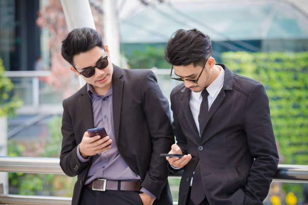 Twee slimme zakenlieden kijken en controleren van hun mobiele telefoon - Foto, afbeelding