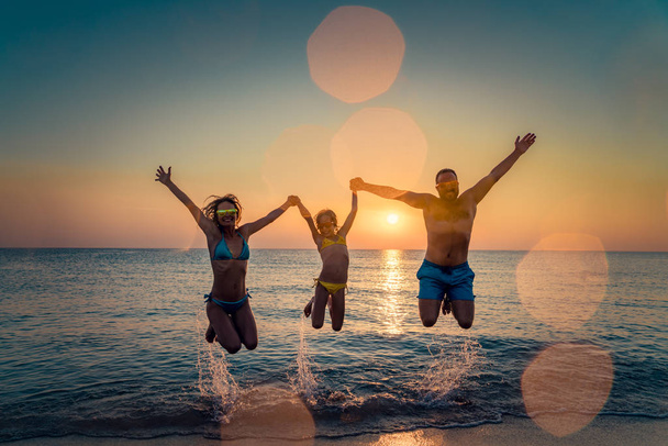 幸せな家族が海でジャンプします。人々 は屋外の楽しい時を過します。夏休みと健康的なライフ スタイルのコンセプト. - 写真・画像