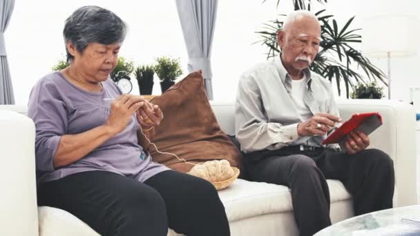 Aasian vanhempi mies, joka käyttää tablet-tietokonetta ja vanhempi nainen neuloo villalla, isoäidit kädet neuloa villalankaa. Craft on vanhojen naisten harrastus ja jolla on polvikipu
. - Materiaali, video