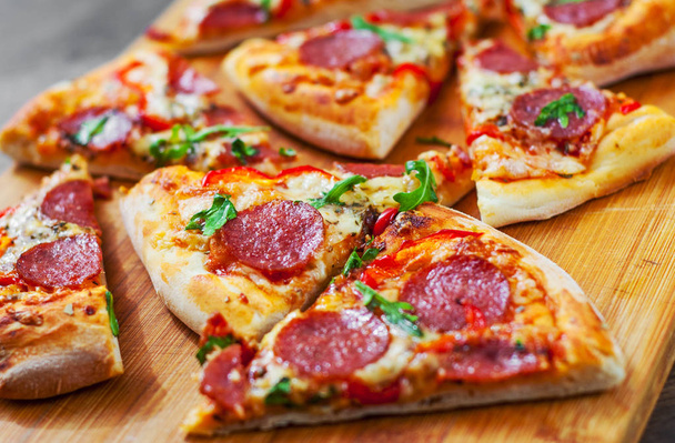 Pepperoni Pizza with Mozzarella cheese, salami, Tomatoes, pepper, Spices and Fresh arugula. Italian pizza on wooden table background - 写真・画像