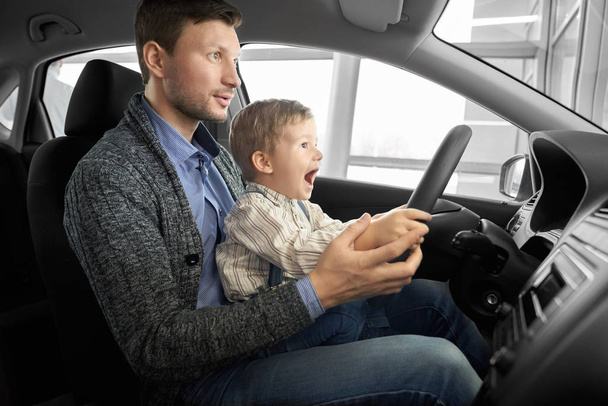 Kleine jongen zitten met vader op bestuurders stoel in nieuwe auto. - Foto, afbeelding