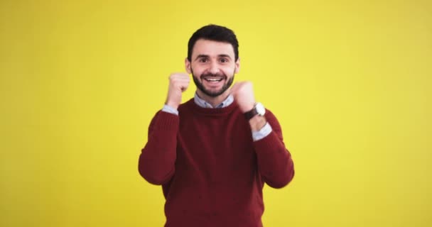 Happy charismatic young man in the studio with a yellow background wall looking straight to the camera smiling large and show a big like - Video, Çekim