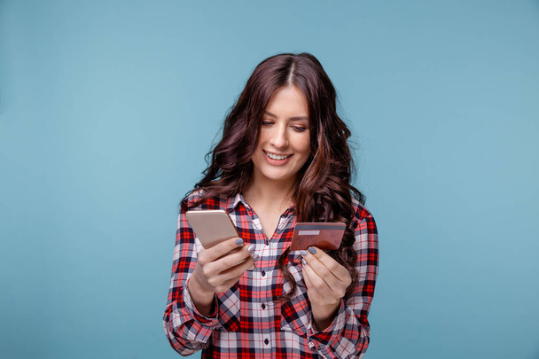 クレジット カードを保持している携帯電話を使用して青の背景に分離された若い女性. - 写真・画像