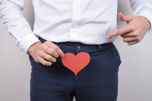 Big large long pleasure intimate intimacy size concept. Cropped close up photo portrait of handsome happy smiling satisfied gentleman showing holding heart near trousers isolated grey background - Photo, Image