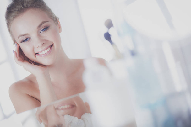Young woman in bathrobe looking in bathroom mirror - Фото, изображение